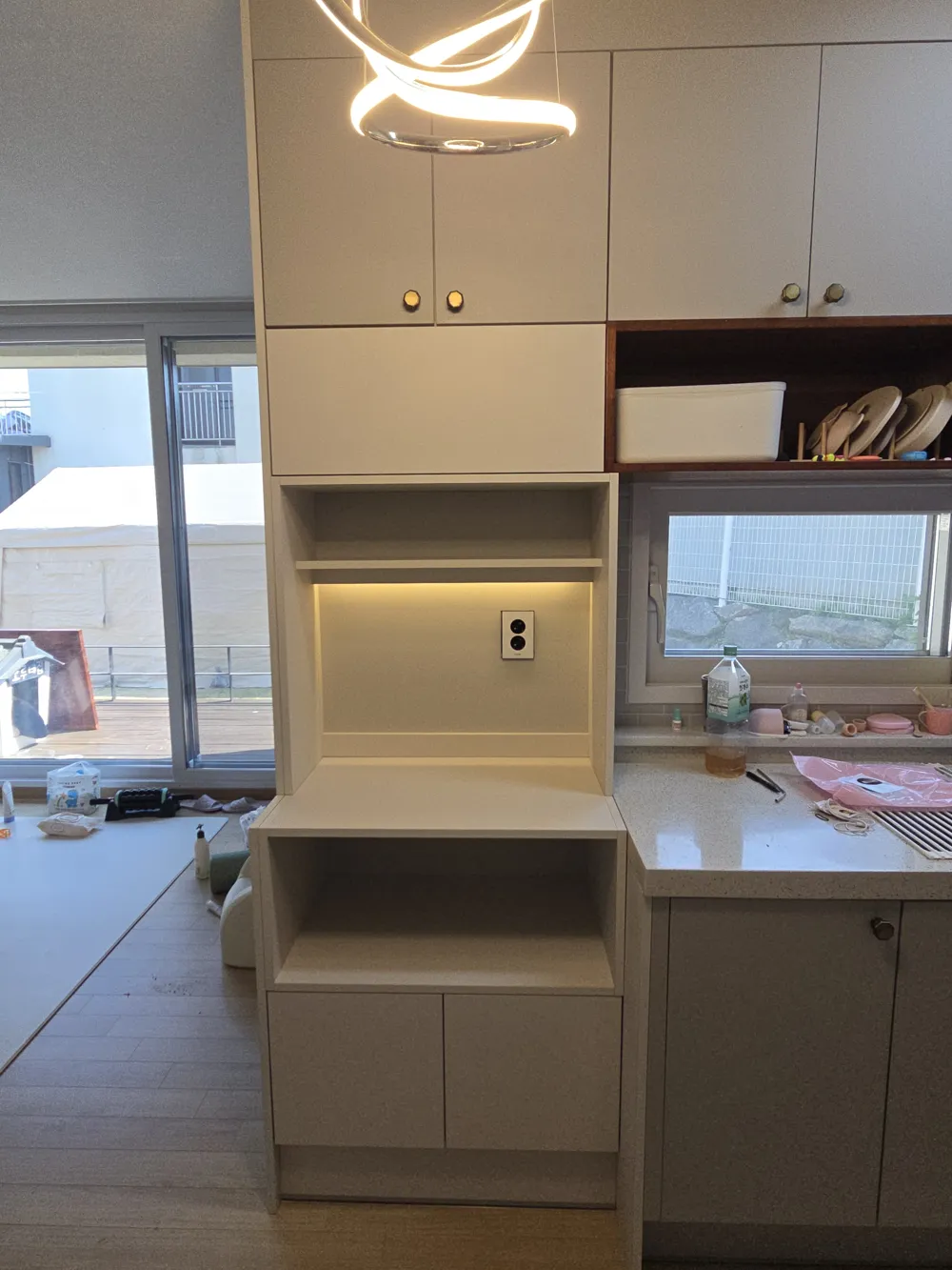 철거한 자리에 시공된 맞춤 수납장으로 상단 도어, 오픈 선반, 간접조명, 콘센트, 하단 도어가 층층이 보이는 사진